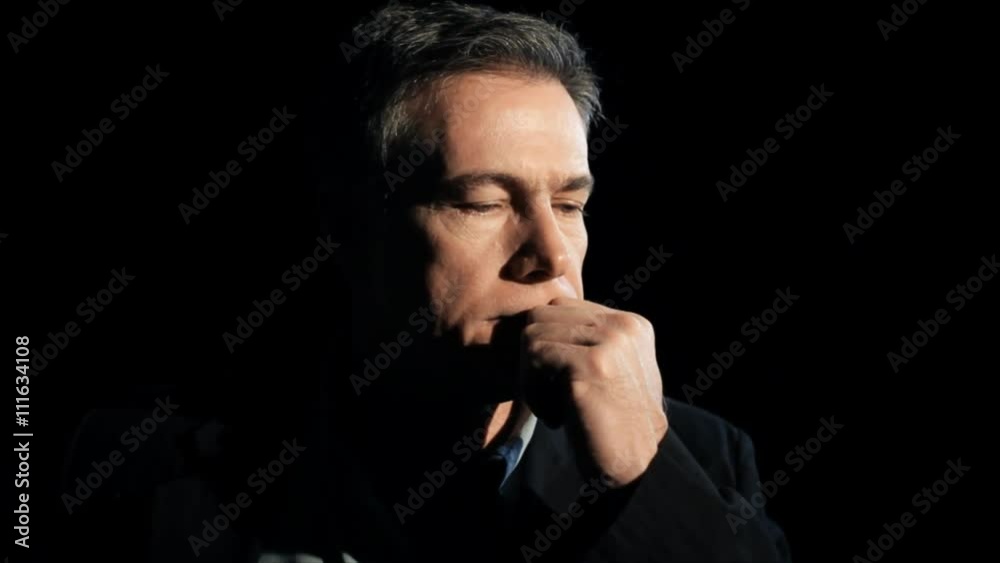 A dark backdrop and harsh lighting frames a mature man who appears rather melancholy. A dark backdrop and harsh lighting frames a mature man who appears rather melancholy.