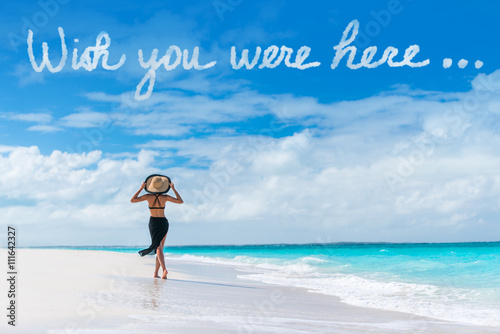 Wish you were here cloud message written in sky above woman walking on beach vacation Luxury travel Caribbean destination. Tourist relaxing on summer holiday at resort. Popular saying postcard.