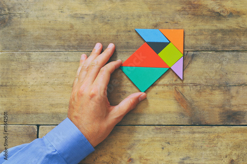 man s hand pointing at arrow made from tangram puzzle