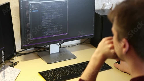 young guy programmer typing on a keyboard code. back view. Focus on the screen.