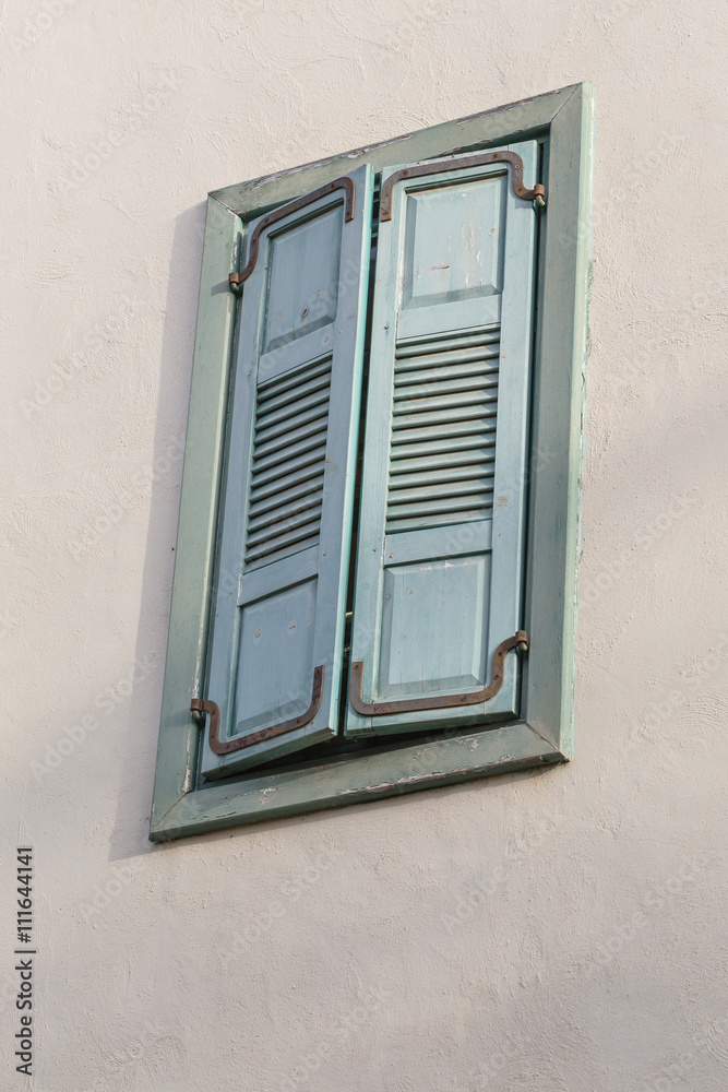 Closed window frame from outside on the wall. Window with wooden green shutters. Evening sunlight.