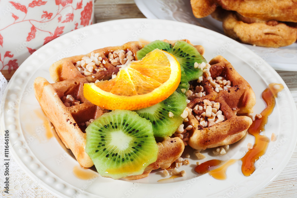 Belgian waffles with orange, kiwi, nuts on a plate close-up