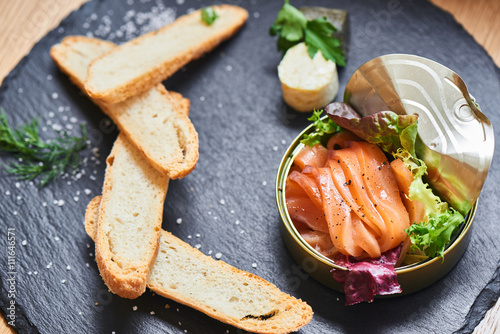 Poorly salted salmon served in a tin and crispy baguette on a stone plaque closeup