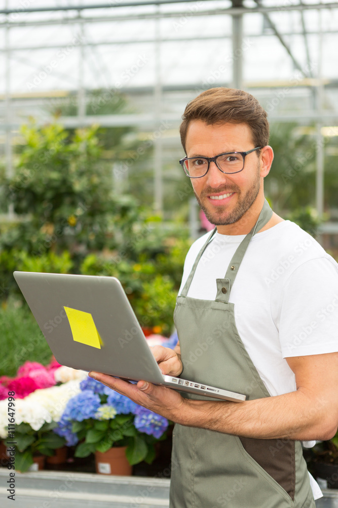 Fototapeta premium Young attractive man working at the plants nursery using laptop