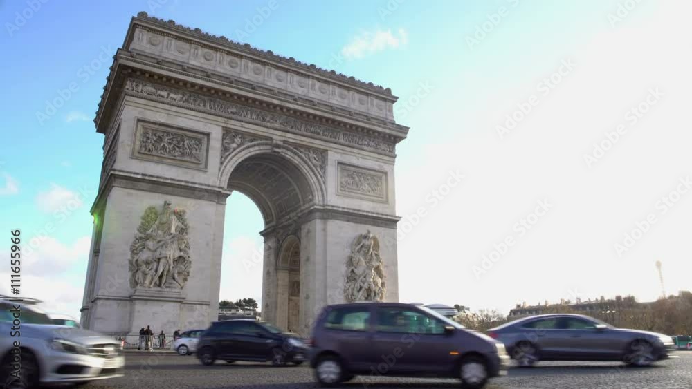 Many cars driving by Arc de Triomphe in sunlit Place Charles de Gaulle in Paris