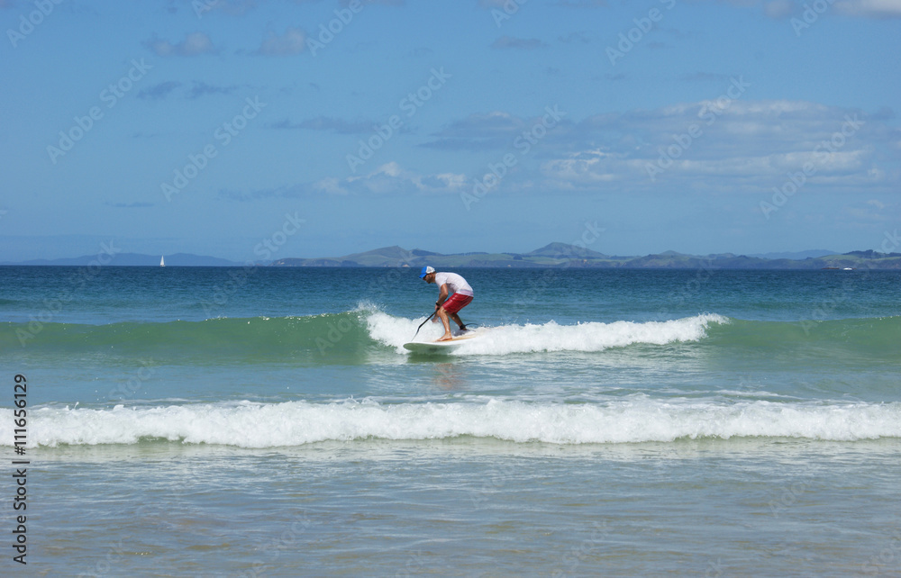 Paddleboarder on a SUP surfing a wave. Paddle boarder photographed in Northland, New Zealand.