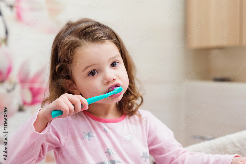 Little girl in pink pyjamas in bathroom brushing teeth