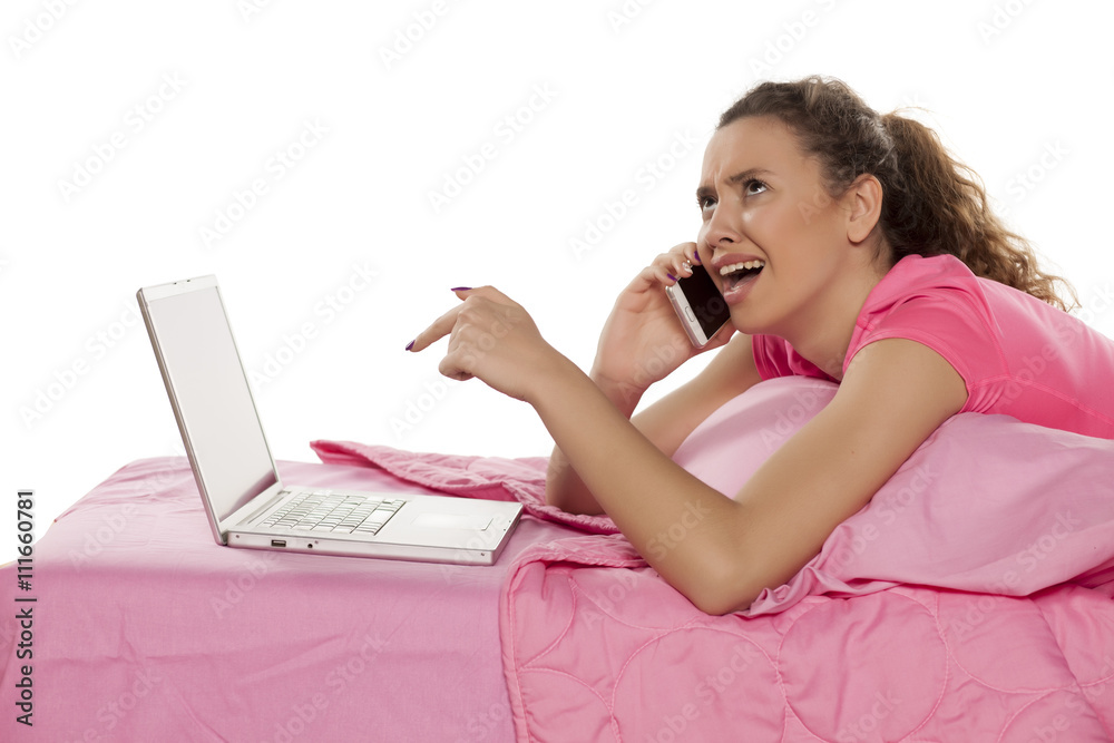 young woman lying in bed with a laptop and complained on the phone young woman lying in bed with a laptop and complained on the phone