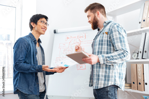 Two confident businessmen making business plan using tablet and flipchart