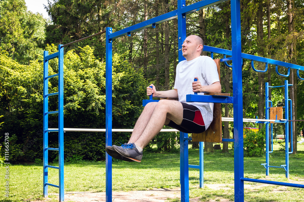 fitness, sport, exercising, training and lifestyle concept - young man doing abdominal exercise in summer park. fitness, sport, exercising, training and lifestyle concept - young man doing abdominal exercise in summer park.
