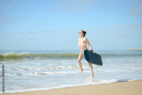 Joyful surfer girl happy cheerful going surfing at ocean beach running into water. Female bikini woman heading for waves with surfboard 