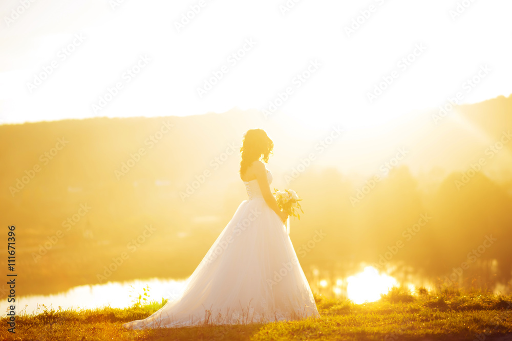 Portrait of a wedding bride posing in a white hipster style dress with flowers in her hands in the forest on sunset