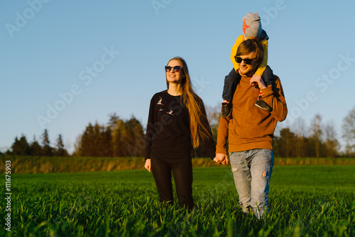 Young parents with a young son walking on a field at sunset in the summer. Concept of family