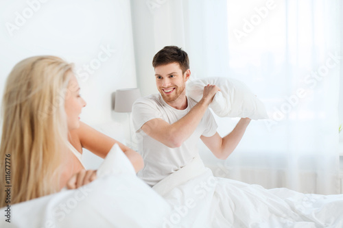 happy couple having pillow fight in bed at home