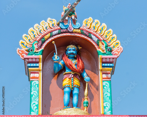 Chettinad, India - October 16, 2013: Ayyanar in a niche at his shrine above entrance gate in Pilivalam village. Blue sky.