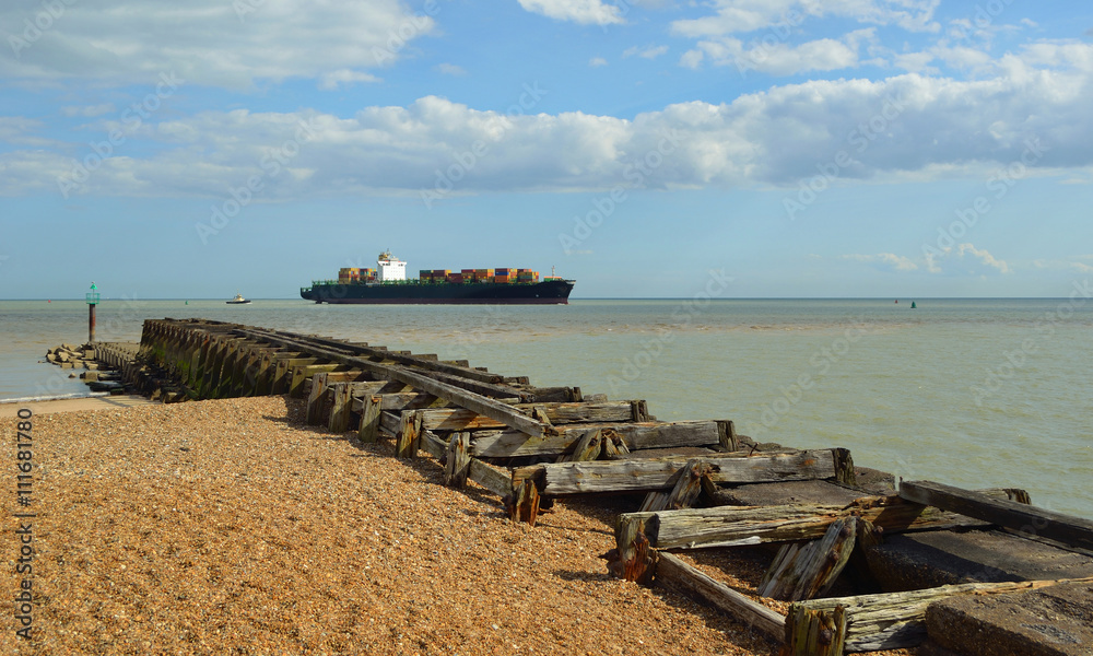  A small Container ship entering the Port of Felixstowe being guided by tug, old breakwater in foreground.