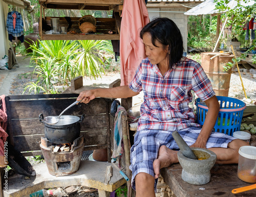 Senior women cooking outdoor, Thai countryside and local lifestyle, mother cooking outdoor sitting in hut with pot and firing firewood in stover