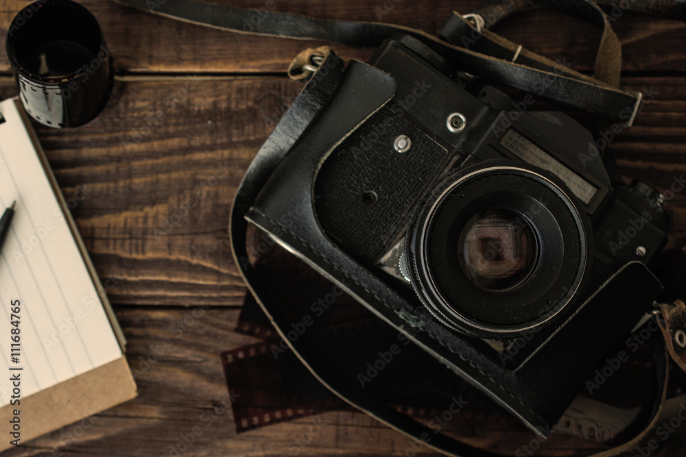 old retro camera with photo film rolls, lined notebook and pen on vintage wooden background. top view