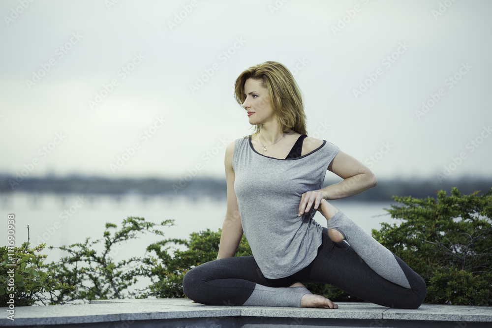 young woman practices yoga on a background of the river