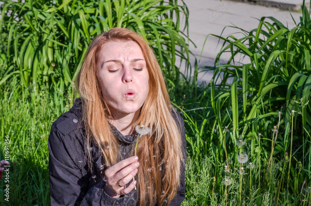 Young charming beautiful girl with long hair Europeans in a meadow with grass and flowers, plucked a flower dandelion and blowing it
