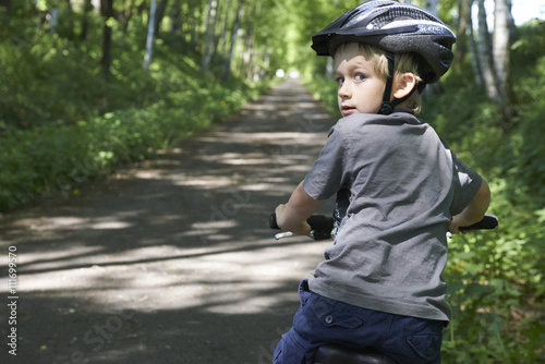 Little Boy riding his bicycle on a dirt road in the woods looking back.