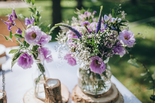 decoration of flowers, herbs and wooden elements on a festive table with a white cloth, which stands on a green lawn in the forest