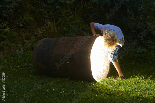 curious child boy looking into glowing hole of barrel