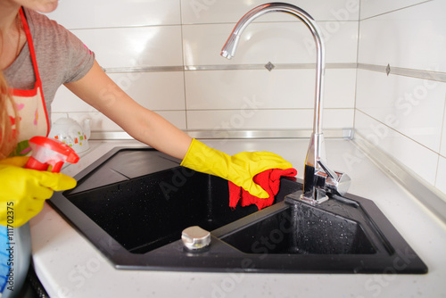 A Woman hand in yellow rubber protective glove cleaning black kitchen sink