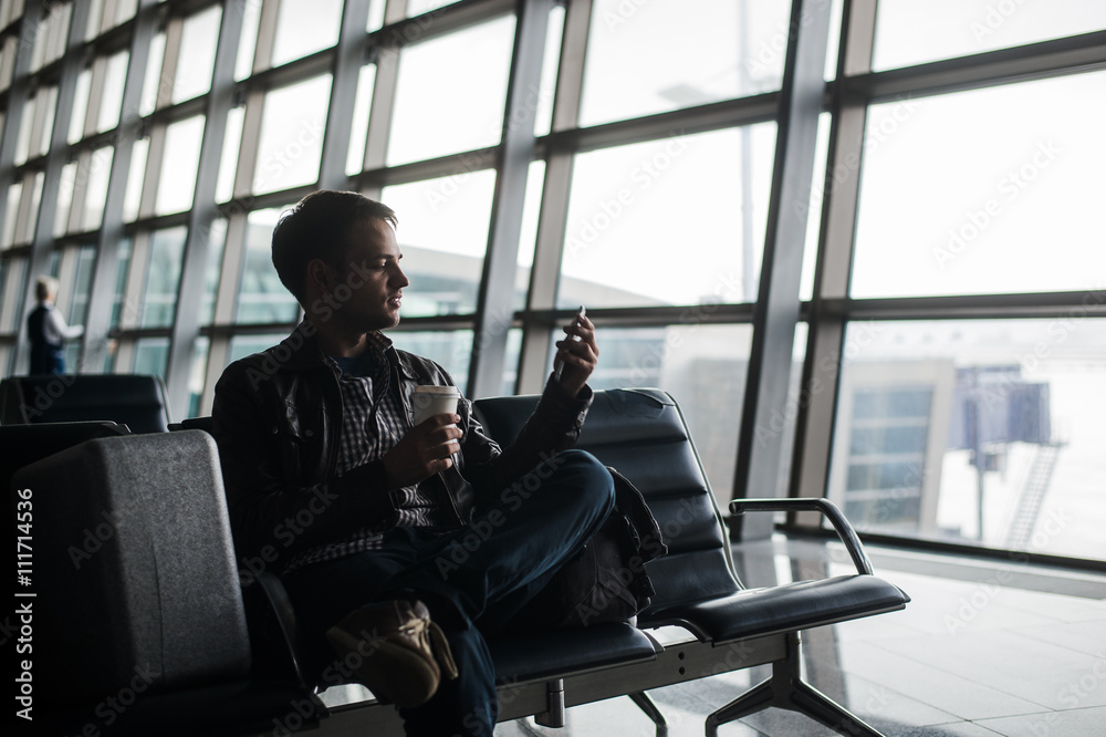 man waiting at airport lounge texting with his smart phone
