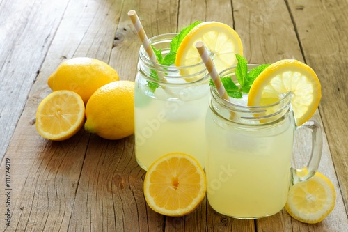 Two mason jar glasses of homemade lemonade on a rustic wooden background