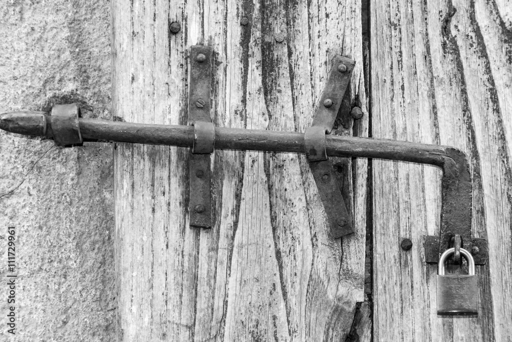 A wooden door locked with a chain and a rusty padlock