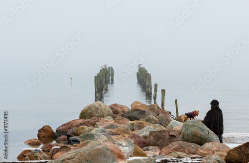 Winter misty coastal landscape with old broken pier and walking woman with a ...