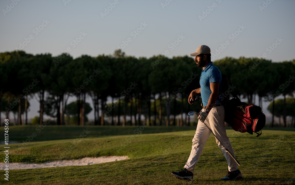 Obraz premium golfer walking and carrying golf bag at beautiful sunset