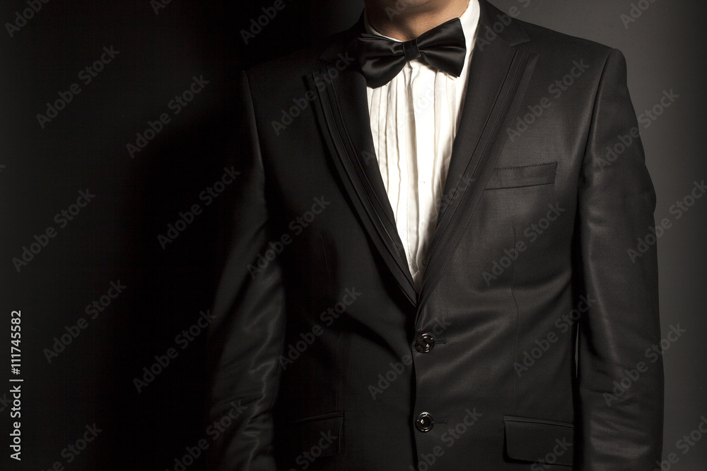 man wearing a black suit and bow tie on black background