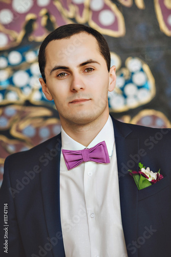 the groom in a blue suit and bow tie posing in the photo