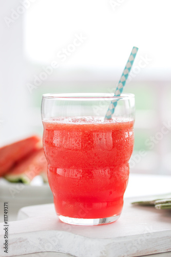 Homemade juicy cold drink with watermelon and water in a glass with blue straw on a wooden cut board, closeup
