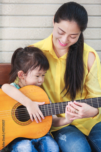 Mother with daughter play guitar. Family spending time together at home. 