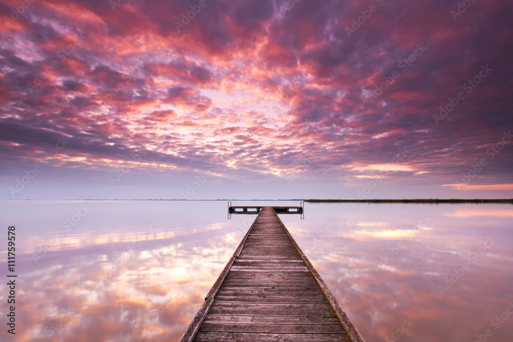 Fototapeta premium Licht durchbricht die Wolken, Sonnenaufgang am See mit Steg