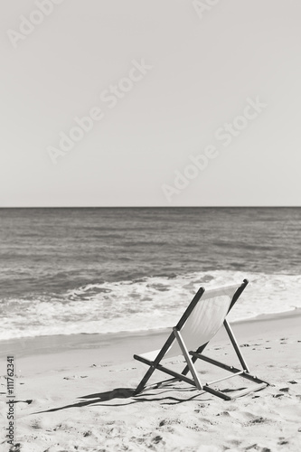 Black and white picture back view of deckchair on a beach, sunny ocean sky outdoors background 