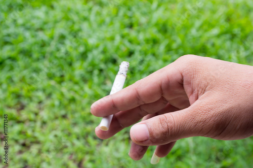 A man holding a cigarette and a smoke and blur green grass background © fangphotolia