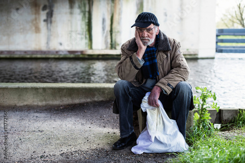 Depressed homeless man sitting on concrete wall under bridge.