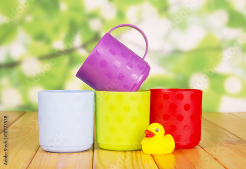 Colorful plastic cups and rubber duck on green abstract background.