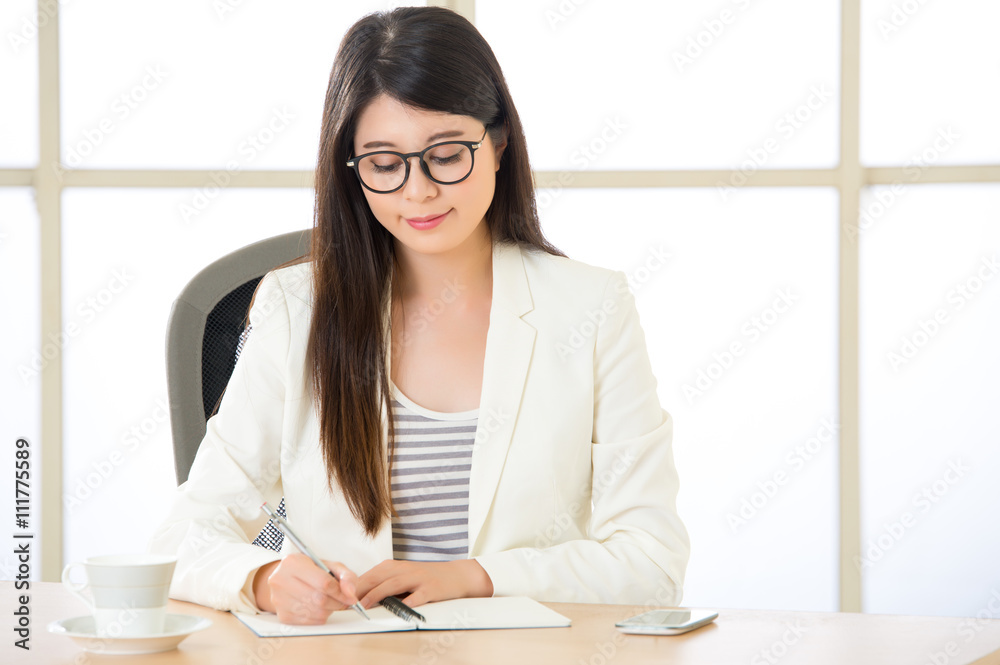 Young Asia businesswoman smiling and writing at desk Young Asia businesswoman smiling and writing at desk