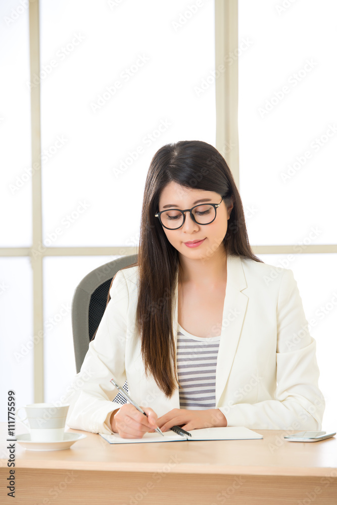 Young Asia businesswoman smiling and writing at desk Young Asia businesswoman smiling and writing at desk