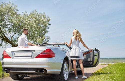 happy man and woman near cabriolet car at sea