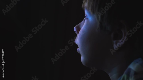 Young boy watching cartoons in a dark room on a computer
