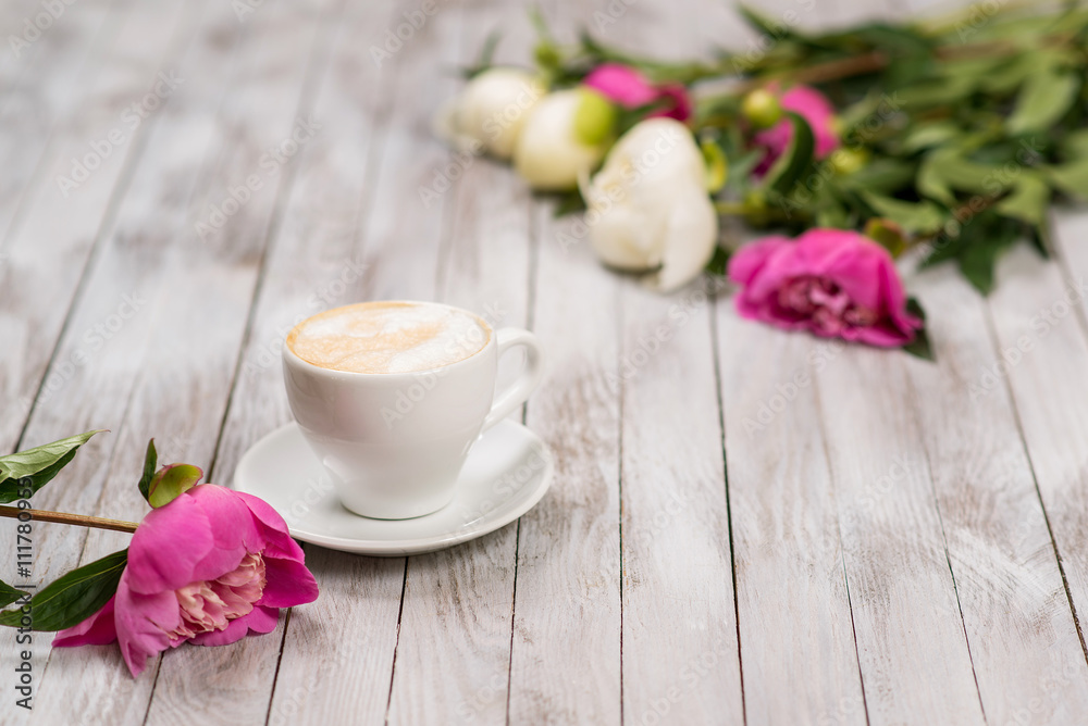 A bouquet of peonies and cup of coffee on a light wooden background.