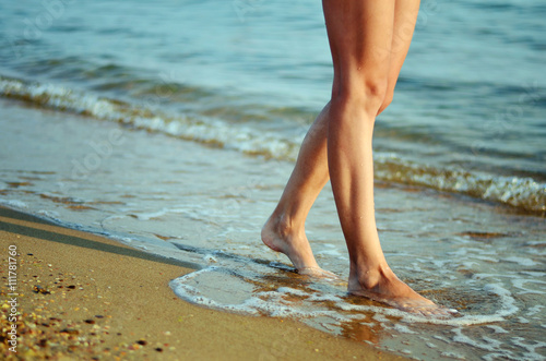 Woman walking along the coast. Feet on the wet sand washed by the waves