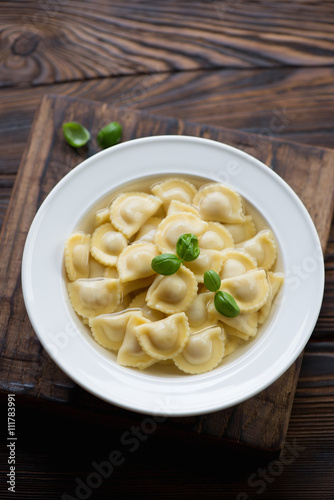 Ravioli in bouillon with green basil, rustic wooden background