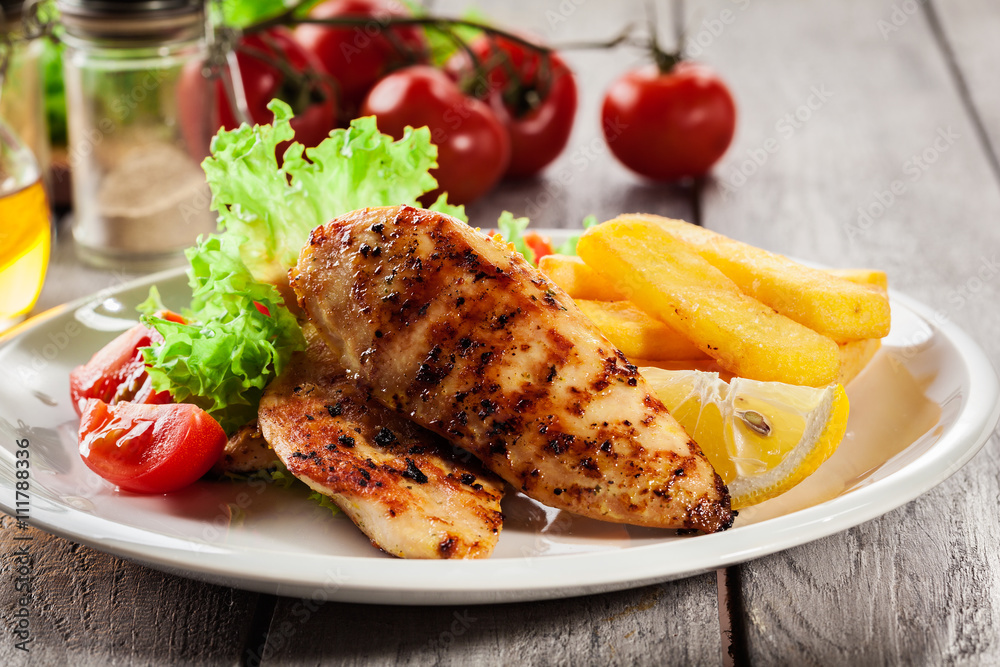 Grilled chicken breasts served with fries and fresh salad Grilled chicken breasts served with fries and fresh salad